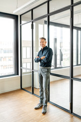 Businessman leaning on glass wall in  his office, with arms crossed