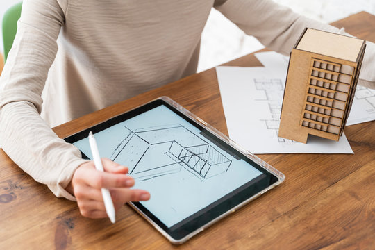 Woman working on architectural model and digital plan on desk in office