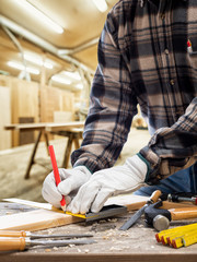 Close-up. Carpenter with his hands protected by gloves with pencil and carpenter's square draw the cutting line on a wooden board. Construction industry, carpentry workshop.