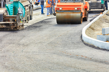 Big and heavy road equipment is working on the construction of a new asphalt road.