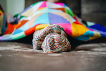 Feet of a woman with socks on a brown sofa covered with a patchwork blanket