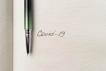Covid-19 coronavirus inscription on a blank empty sheet of paper in a notebook. Nearby lies a pen. A lot of space for inscriptions and copyspace. Blank for inscriptions. Template for article or cover.