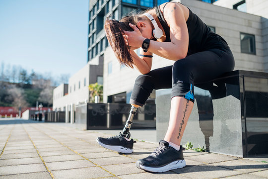 Exhausted sporty young woman with leg prosthesis in the city