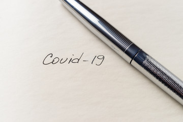 Covid-19 coronavirus inscription on a blank empty sheet of paper in a notebook. Nearby lies a pen. A lot of space for inscriptions and copyspace. Blank for inscriptions. Template for article or cover.