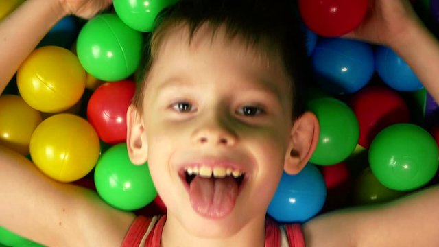 Happy cute boy jumps his head in inflatable balloons at a children's birthday party. Children's amusement park. Children's playroom in the entertainment center