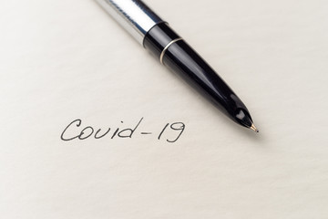 Covid-19 coronavirus inscription on a blank empty sheet of paper in a notebook. Nearby lies a pen. A lot of space for inscriptions and copyspace. Blank for inscriptions. Template for article or cover.