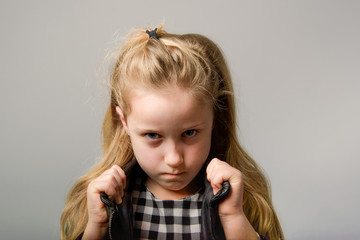 Angry and stubborn little slavic kid girl in leather black jacket on grey background.