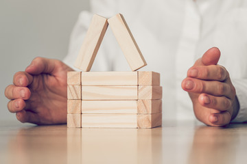 Real estate, home insurance concept - hands abstractly protect a house from wooden blocks.