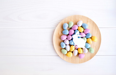 Easter background with colorful eggs and paper bunny silhouette on wooden plate. White wooden rustic background. Happy Easter. Space for text. Place for text