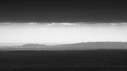 Telephoto view of the hills in the distance, covered by fog.  Monochrome image from the Malvern Hills, UK