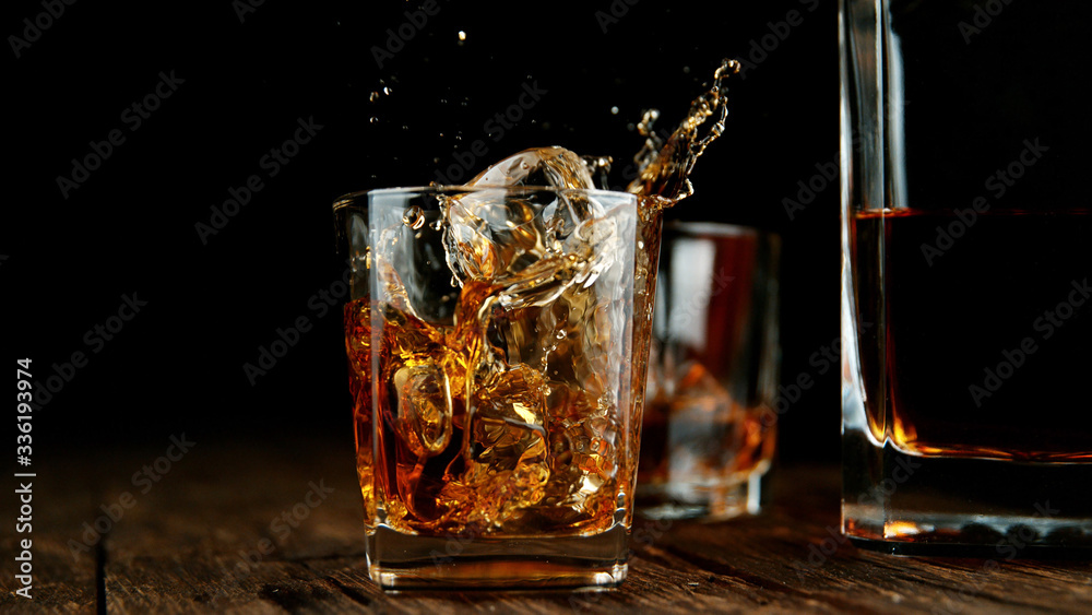 Poster splashing whiskey from glass with ice cubes inside