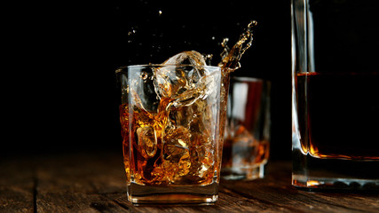 Splashing whiskey from glass with ice cubes inside - obrazy, fototapety, plakaty