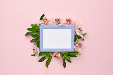photo frame decorated with green leaves and orchid flowers on pink pastel background. empty space...