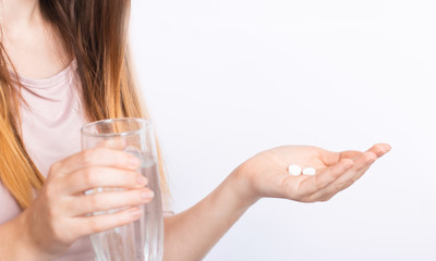 Woman feels sick, holds pills and a glass of water in detail on a white background. The concept of headache, migraine, pain reliever, respiratory disease, flu, vitamins and fever, covid-19