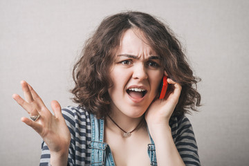 Woman talking on a cell phone, bad news surprised. Gray background