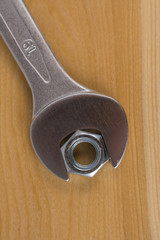 Metalowy klucz, oraz nakrętka ułożone na drewnianej desce.