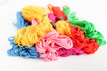 Many mixed vivid colored sewing threads for embroidery isolated on a white table, top view or flat lay of red, pink, yellow, blue and green textile materials
