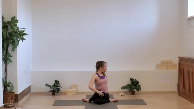 A yoga teacher in a pilates studio on a yoga mat shows the correct twist to the left in the pose of the king of fish. Ardha Matsyendrasana