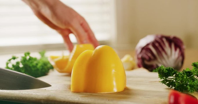 Close Up slow motion shot of a man chopping a yellow pepper as he makes a healthy salad at home in the kitchen.