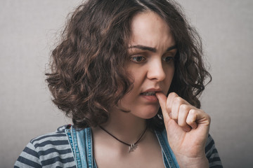 Woman bites his nails from the experience. On a gray background.