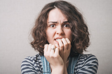 Woman bites his nails on the experiences of fear. On a gray background.