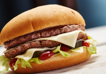 Close-up of delicious fresh home made burger with lettuce, cheese, onion and tomato on a rustic wooden plank on a dark background.