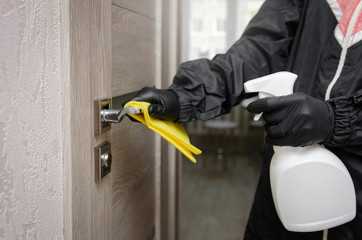 
Disinfection, cleaning and washing of door handles in overalls and a mask. COVID-19. Prevention of coronavirus infection. closeup of a disinfecting the door handle by spraying a sanitizer from a whit