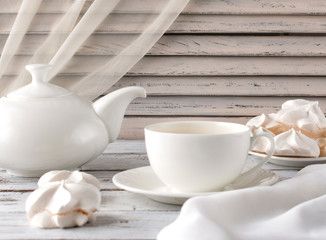 Cup of tea and teapot on an old white table. White morning with marshmallows sweets