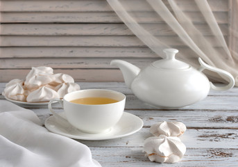 Cup of tea and teapot on an old white table. White morning with meringues sweets