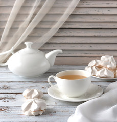 Cup of tea and teapot on an old white table. White morning with meringue sweets