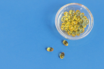 Yellow gelatin capsules with vitamin D3 in a glass container on a blue background. Pharmaceutical therapeutic and prophylactic preparation of vitamin D deficiency in adults and children.