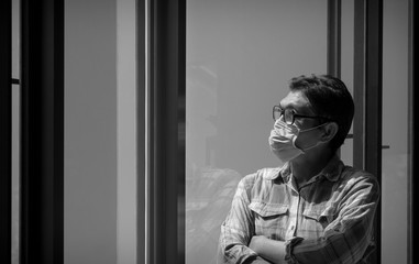 Asian man in plaid long sleeve shirt  wearing protective mask and looking out of the glass window at home, He hopes that the spreading of the Coronavirus problem will end soon, black and white style
