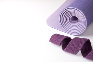 Fototapeta na wymiar Accessories for yoga, pilates or fitness. Purple yoga mat and purple belt on a white background with copyspace