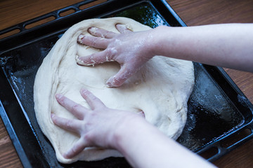 Picture of a person stretching a pizza dough on a baking tray from the oven, top view