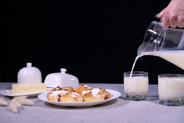 Pouring cow's milk into a glass on a gray wooden table with homemade cookies. Delicious breakfast concept