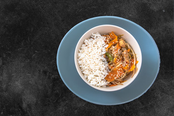 Comida oriental en bowl blanco con fondo negro.