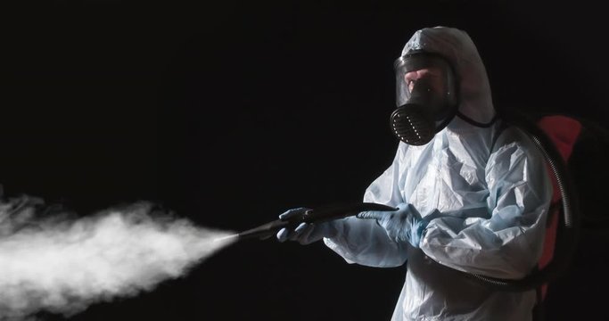 Caution Disinfection is in Progress. A man in a protective suit, glasses and a respirator sprays a disinfectant. At the same time, he makes gestures symbolizing the ban on presence
