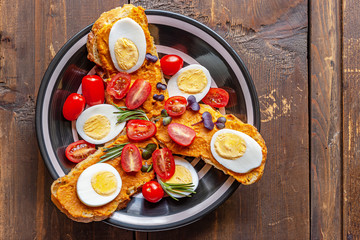Bruschettas of dietary bread with vegetable puree and boiled eggs decorated with cherry tomatoes and young herbs top view