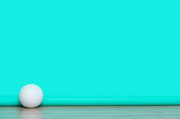 Volleyball lying on wooden surface near mint color wall with copy space