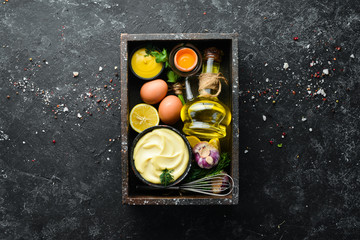 Cooking mayonnaise sauce. Oil, mustard and eggs. Culinary black stone background. Top view.