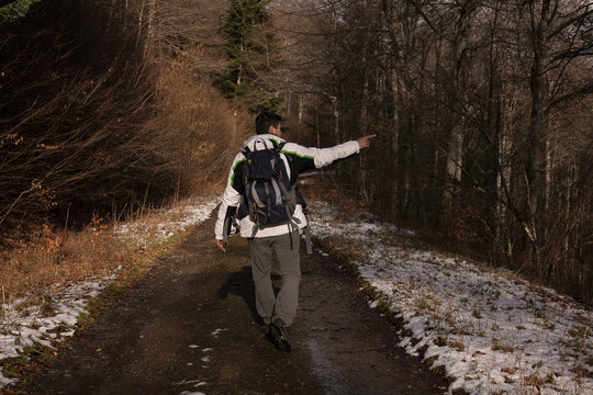 A man with a bagpack is hicking in Giromagny winter forest, and he is showing something 