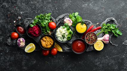 Set of colored sauces and spices on black stone background. Traditional sauces for meat and fish.