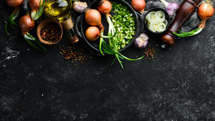 Culinary background. Onions, garlic and spices on a black stone background. Top view.