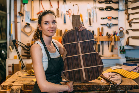Young Woman Luthier holding a guitar template while looking at c