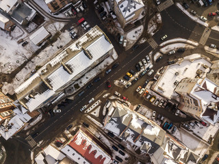 Aerial black and white winter top view of modern city with tall buildings, parked and moving cars along streets with road marking. Urban cityscape, view from above.