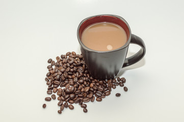 Coffee in a mug sitting beside a pile of beans against a white background