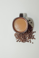 Coffee in a mug sitting beside a pile of beans against a white background