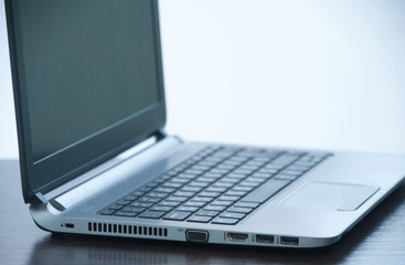 Silver modern laptop on a brown wooden table. Side view. Work concept