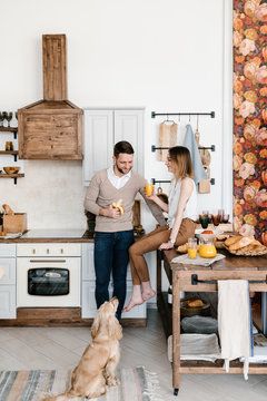 Couple have breakfast at kitchen with cute dog near.