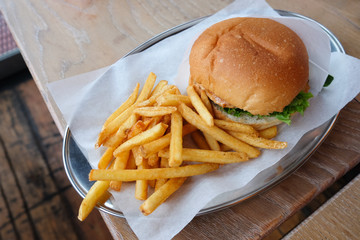 Burger and french fries on parchment paper, on tin dish, on wooden table in cafe, close-up. Concept cheatmeal, malnutrition, junk food, delivery. Horizontal, side view